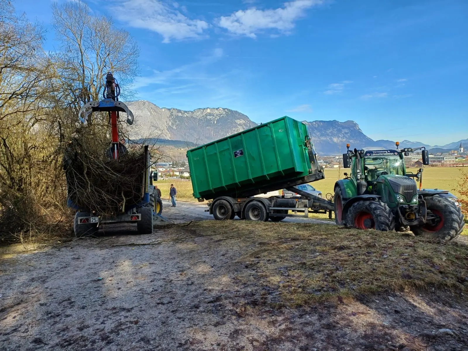 Grüner Holzcontainer und Traktor vor Tiroler Bergen